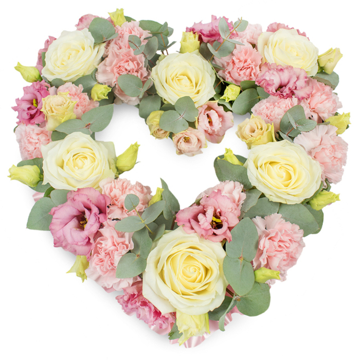 A full, symmetrical heart-shaped wreath of pastel flowers is set against a bright white background, each bloom placed so carefully that the entire piece feels like a soft embrace frozen in time. The heart is entirely filled with flowers, with no visible gaps, giving a dense, lavish appearance that suggests time, skill, and genuine care. Dominating the design are large, creamy ivory and pale buttery-yellow roses, their petals tightly coiled in the centres and then relaxing outward into perfectly cupped blossoms. These roses act as gentle anchors across the heart, representing purity, devotion, and deep affection. Between them, countless clusters of light pink carnations are woven through, their ruffled, almost feathery petals lending a delicate texture, reminiscent of the soft, early spring light that falls over Denmark Hill's quiet residential streets. Intermingled with the carnations and roses are deeper pink to mauve lisianthus flowers, their more open, satin-like petals and occasional darker throats introducing depth and visual interest, much like the shifts of colour you notice walking from Denmark Hill station towards Camberwell Green at dusk. Silvery-green eucalyptus leaves with round, slightly matte foliage frame and thread through the flowers, creating a gentle, cool contrast that calms the palette and suggests a sense of peace. Small yellow-green buds peek from between the larger blooms, symbolising new beginnings and the continuity of life. The overall effect is one of tender remembrance and heartfelt condolence: a classic heart tribute suitable for funerals, memorials, or anniversaries, ideal for families in Denmark Hill who wish to honour a loved one with something both elegant and deeply expressive.